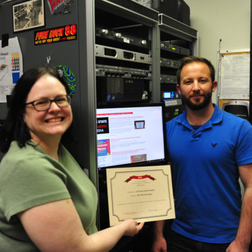 Two people standing in front of a computer holding an award