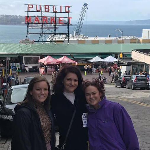 Three women stand in front of Public Market sign in Seattle